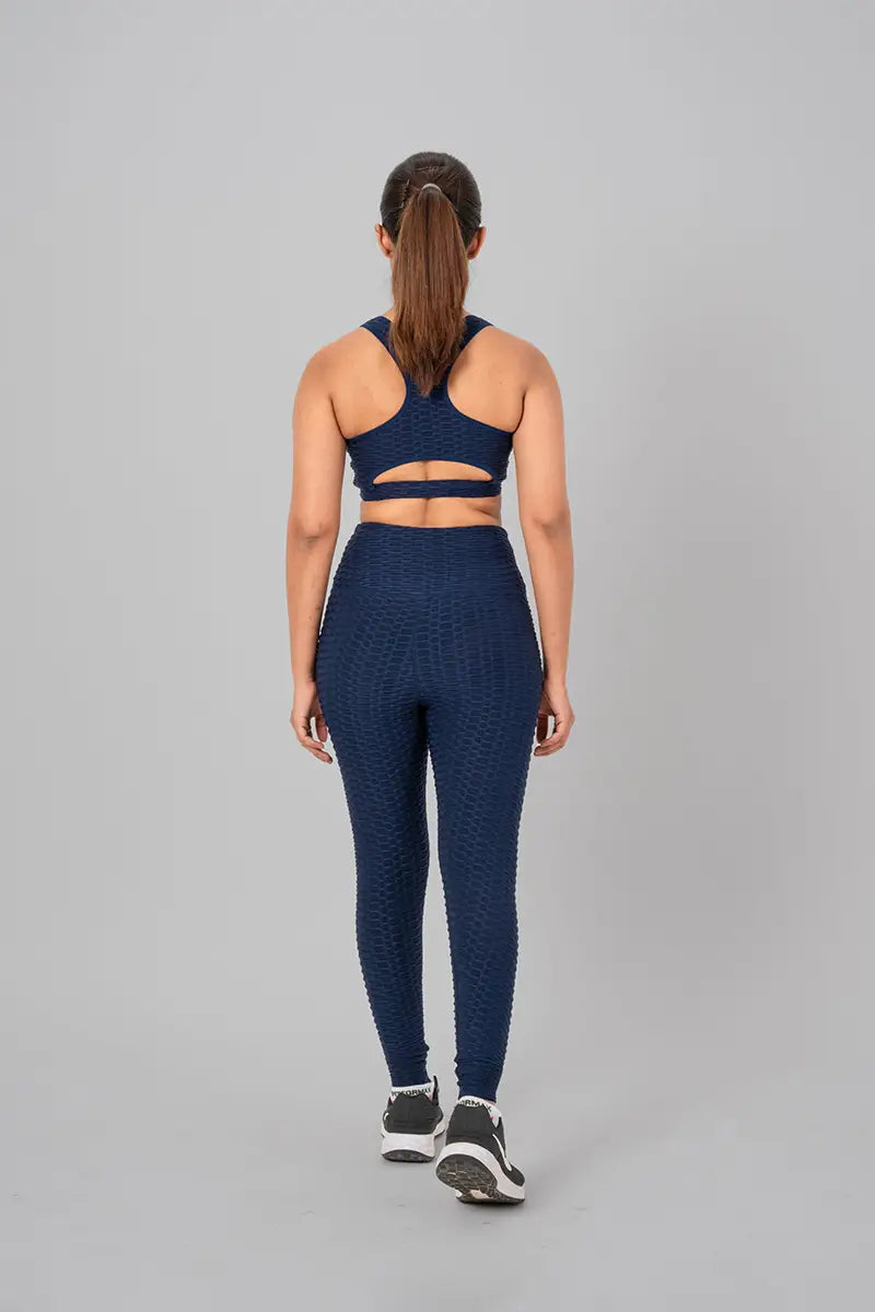 Woman in activewear set, navy blue coord - back view standing, highlighting open back keyhole design and high-waisted support.