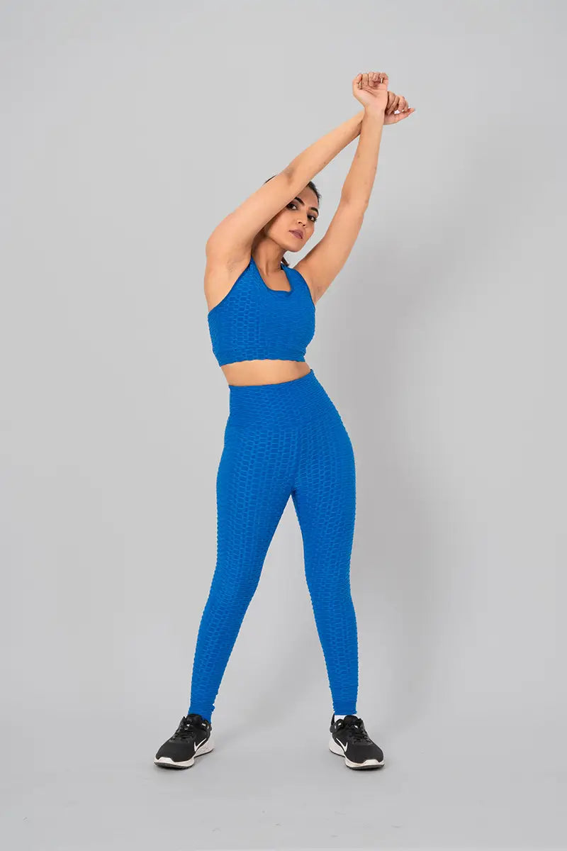 Woman in gym outfits, teal blue coord set - overhead stretch pose emphasizing flexibility and high-waisted support.