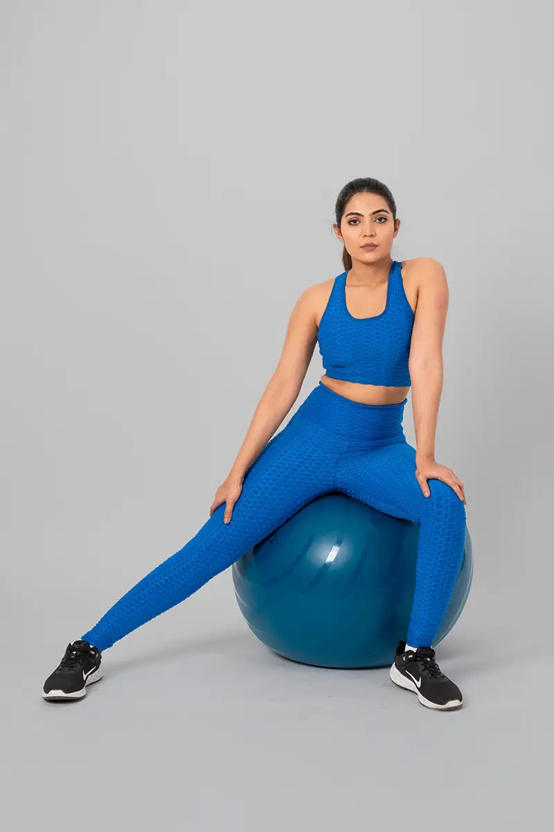 Woman in gym outfits, teal blue coord set - sitting on an exercise ball, demonstrating comfort and flexibility.