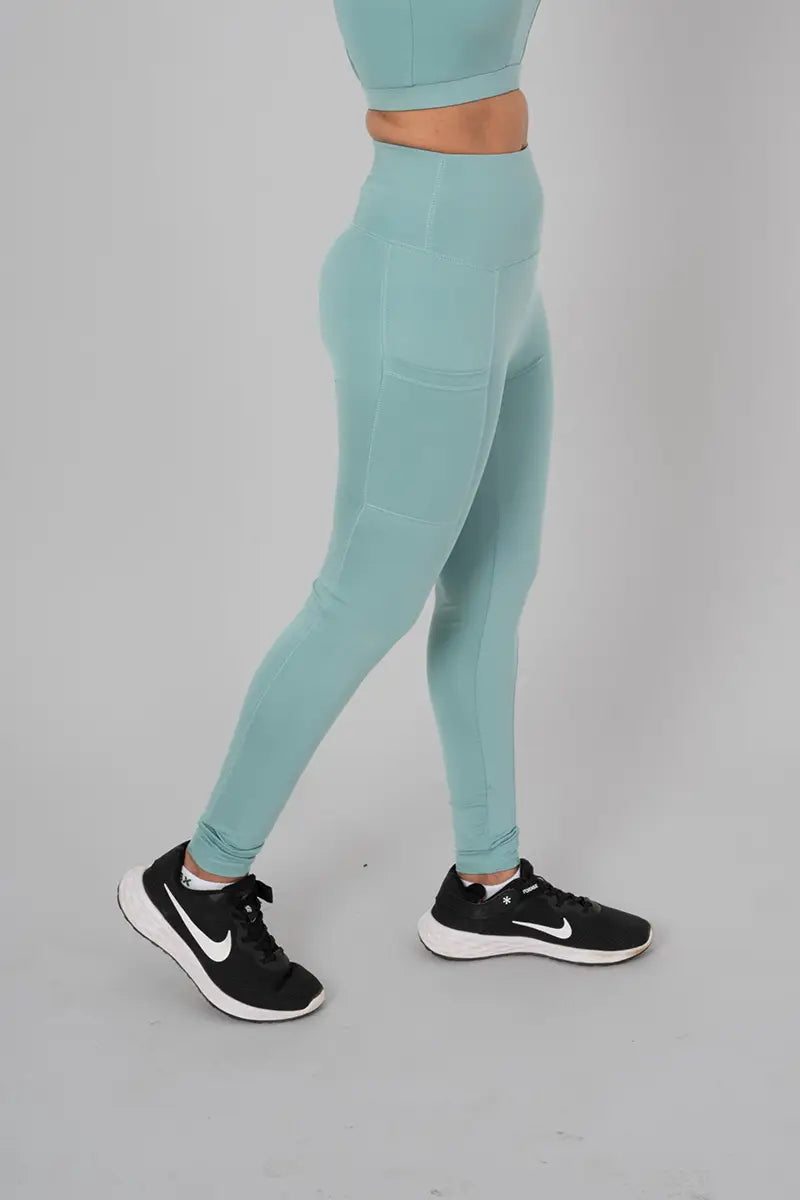 Young woman in activewear pants, mist - side walking pose highlighting squat-proof material and pocket design.