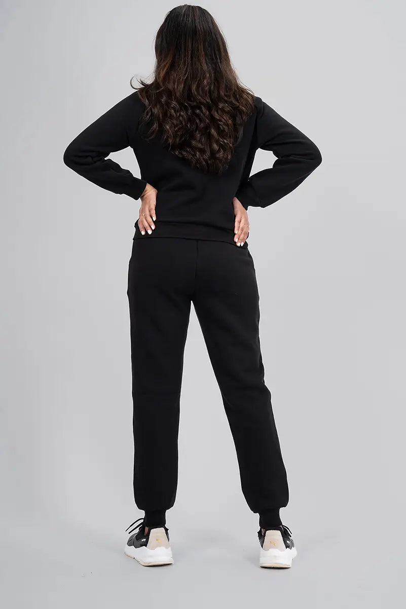 Women's gym pants for winter season, black jogger - back view with hands on waist showing relaxed fit and full coverage.