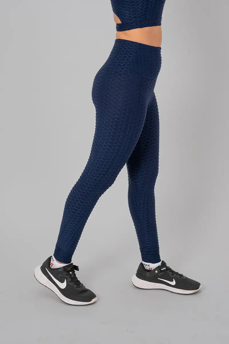 Woman in workout clothes, navy blue leggings - side walking pose showing stretchable fabric and high-waisted design.