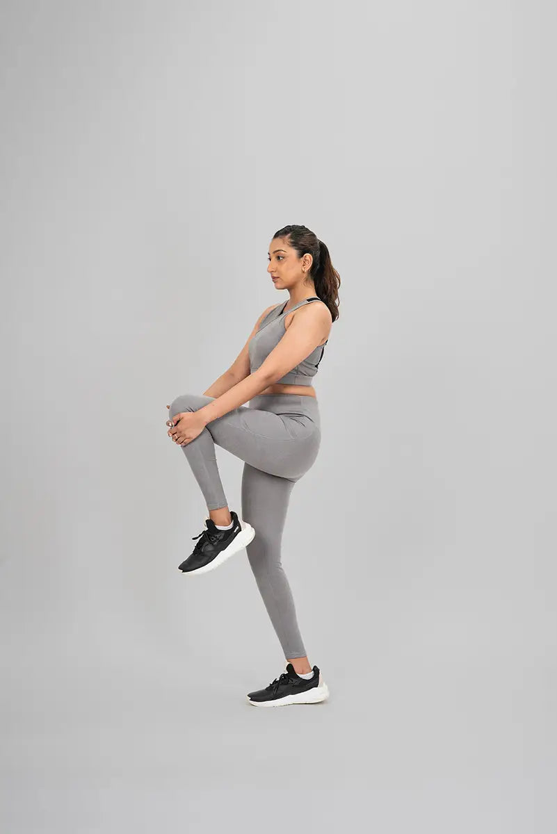 Woman in workout leggings, grey metallic - high knee stretch pose highlighting flexibility and stretchable fabric.