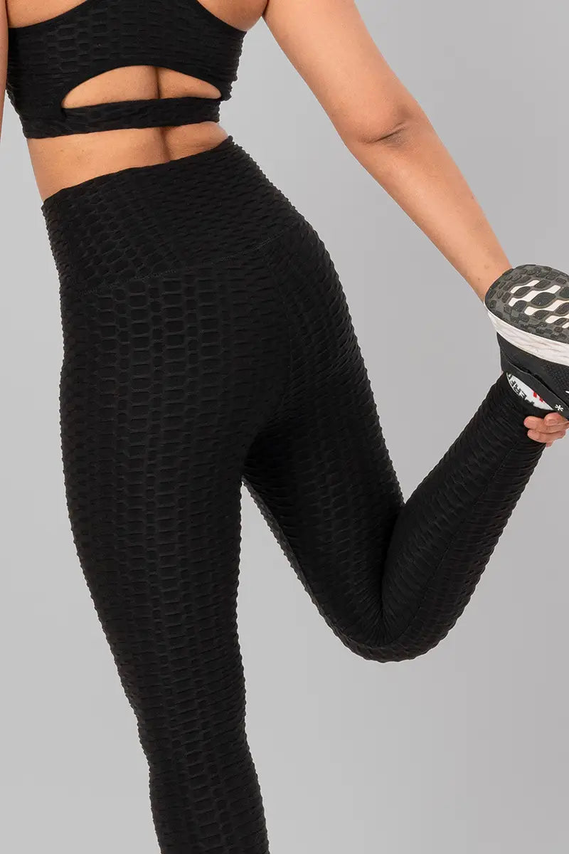 Woman in workout leggings, black - leg pull stretch demonstrating stretchable and breathable fabric.@@@color_Black