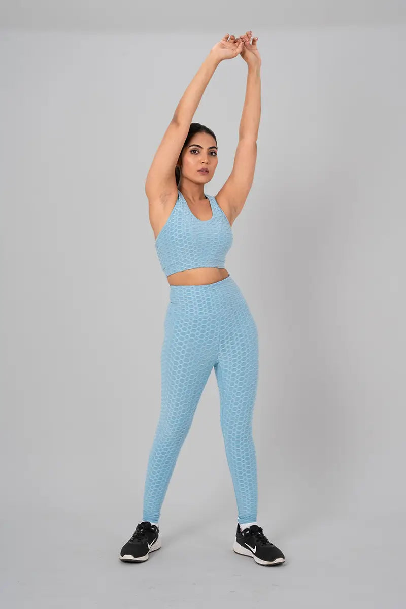 Woman in gym wear sets, sky blue coord set - overhead stretch pose emphasizing stretchable fabric and high-waisted fit.